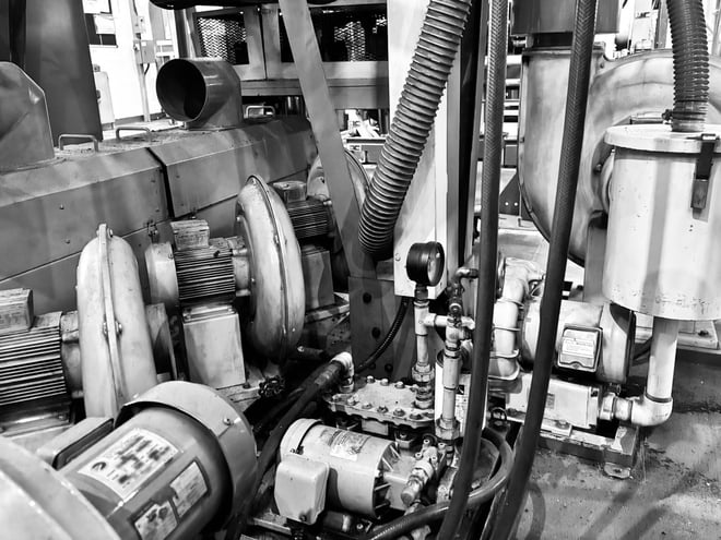 Black and white view of an industrial air compressor system featuring motors, heavy-duty hoses, and pressure gauges, highlighting the complex mechanical components that require routine maintenance