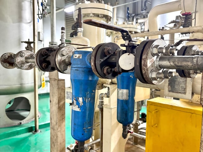 Close-up of blue inline filter housings, flanged connections, and manual valves in an industrial compressed air system, illustrating components where clogs and contamination frequently occur