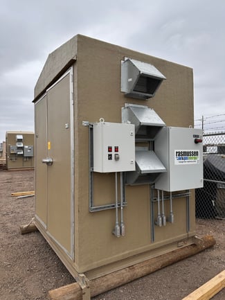 A custom-engineered outdoor enclosure built by Rasmussen Air &amp; Gas Energy, featuring external ventilation and mounted electrical control panels, ready for deployment at a remote industrial field site.