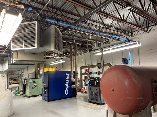 A complete industrial compressed air system showing a Quincy compressor, air receiver tank, and overhead ventilation.