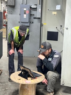 Two Rasmussen Air &amp; Gas Energy technicians analyzing a compressed air system demand profile on a tablet during a facility assessment.