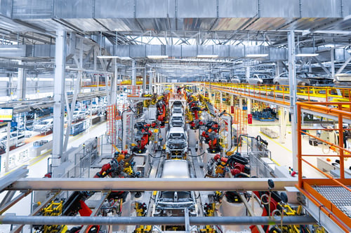 A wide view of a modern automotive manufacturing plant featuring a continuous production line and robotic assembly cells powered by compressed air.