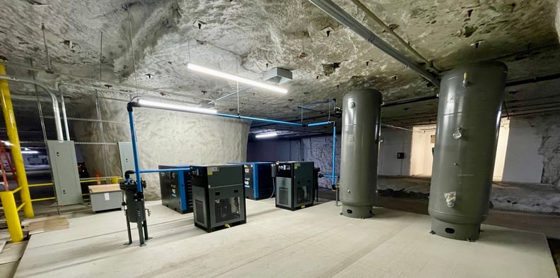 An industrial compressed air system installation showcasing air compressors and two large vertical air receiver tanks for system storage.