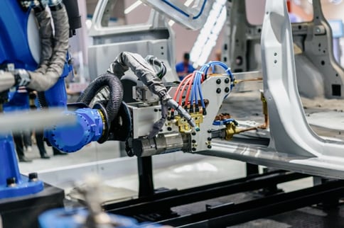 Close-up of a blue industrial robot using pneumatic actuators to assemble a vehicle chassis, relying on stable pressure from an automotive compressed air system